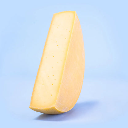 Half wheel of raclette cheese on blue background