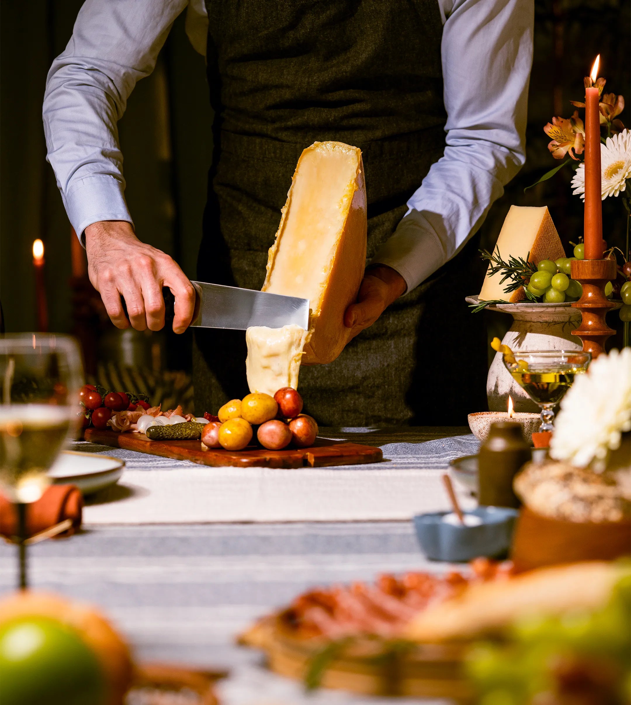 person scraping with melting cheese over potatoes on a cutting board