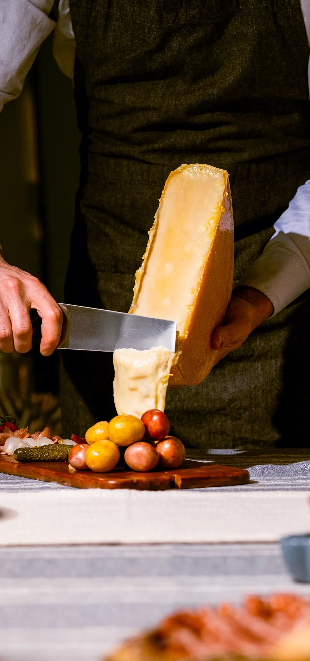 cheese knife scraping melted cheese down a wheel